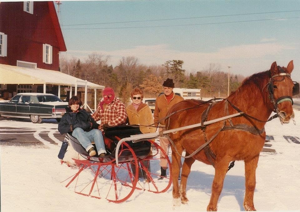 A horse-drawn sleigh in the snow beside the red barn